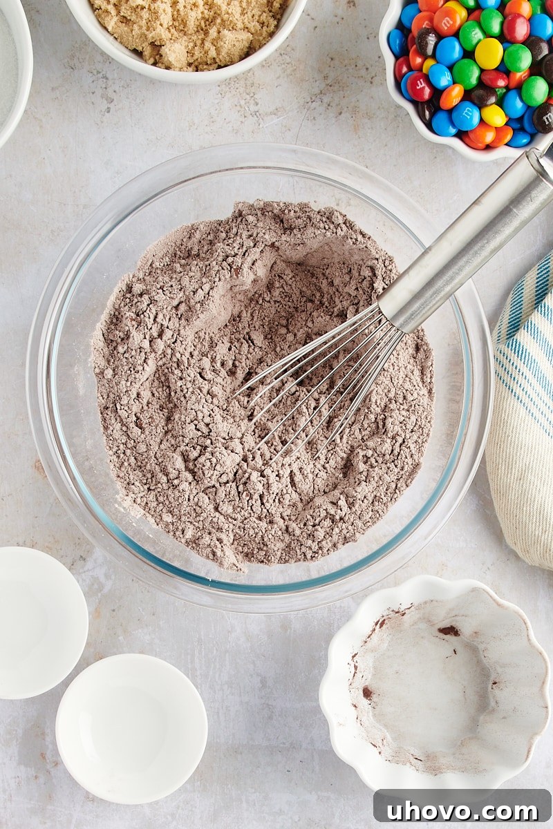 Overhead view of perfectly mixed dry ingredients for Chocolate M&M Cookies in a glass mixing bowl, light brown in color.