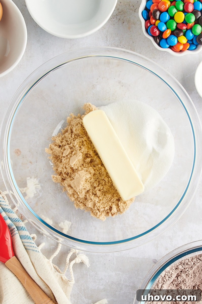 Overhead view of softened butter, granulated sugar, and light brown sugar creaming in a glass mixing bowl.