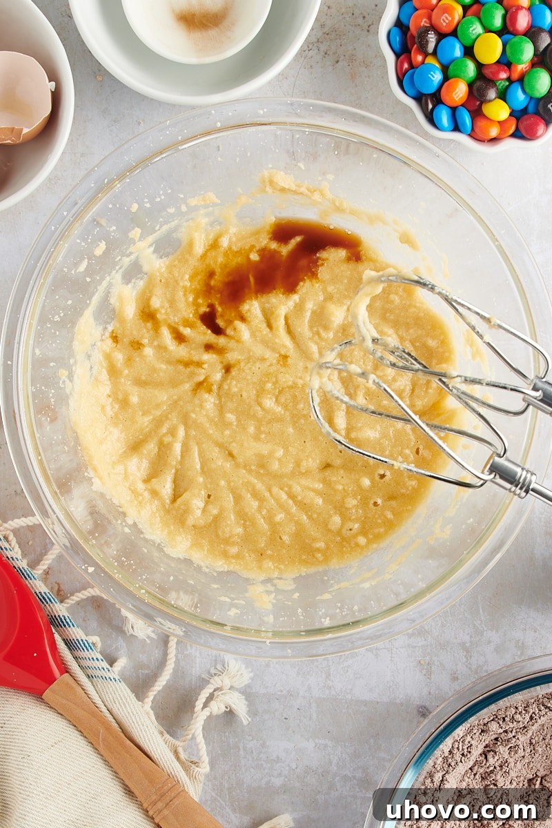 Overhead view of vanilla extract being streamed into the wet ingredients for Chocolate M&M Cookies.