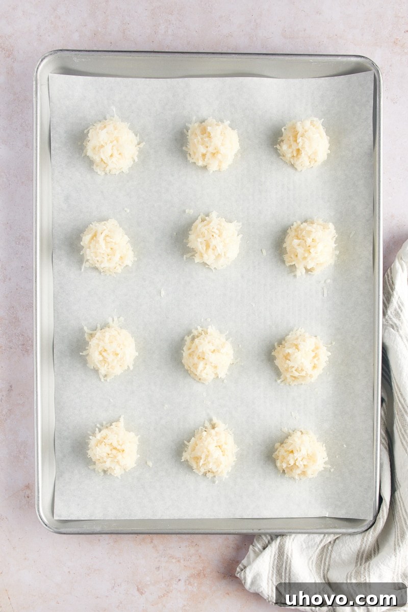 An overhead view of neatly portioned Coconut Macaroons, shaped into perfect domes, arranged on a parchment-lined baking sheet and ready for the oven.
