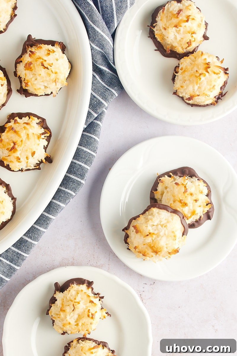 An elegant arrangement of Coconut Macaroons, some plain and some chocolate-dipped, presented on small white plates and a large oval tray, showcasing their versatility.