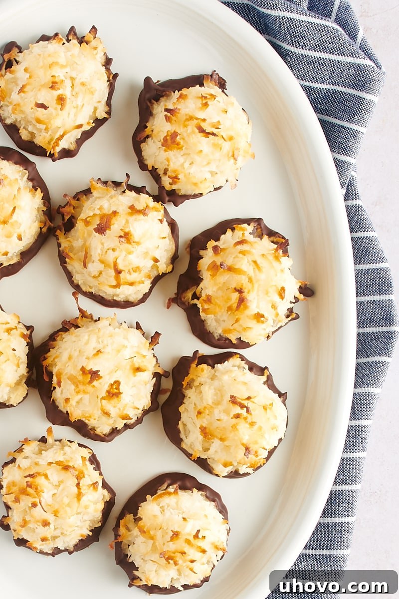 An overhead view of a bountiful pile of golden-brown Coconut Macaroons, uniformly shaped and perfectly baked, artfully arranged on a large white plate.