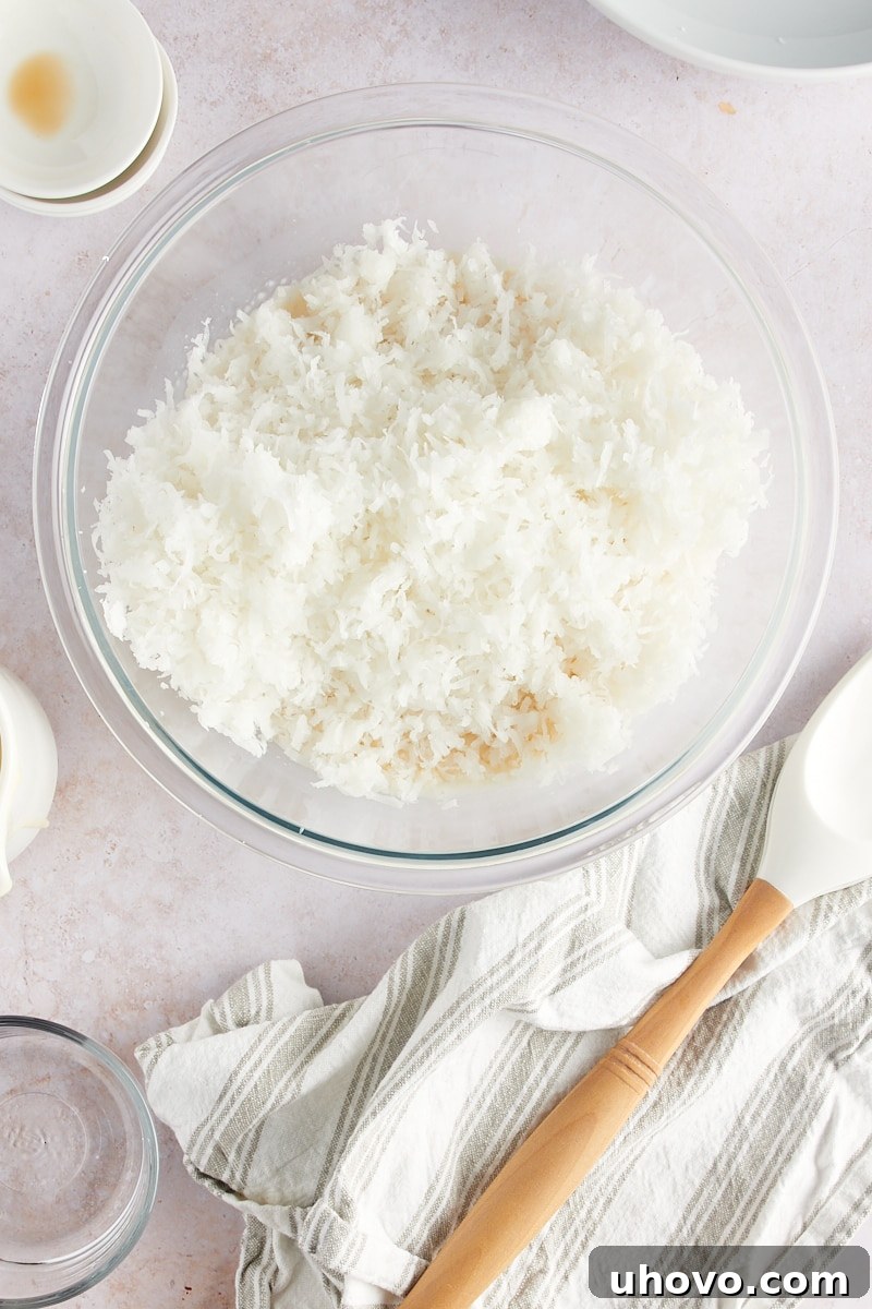 An overhead view of shredded coconut freshly added to the creamy batter for Coconut Macaroons in a glass mixing bowl, awaiting folding.