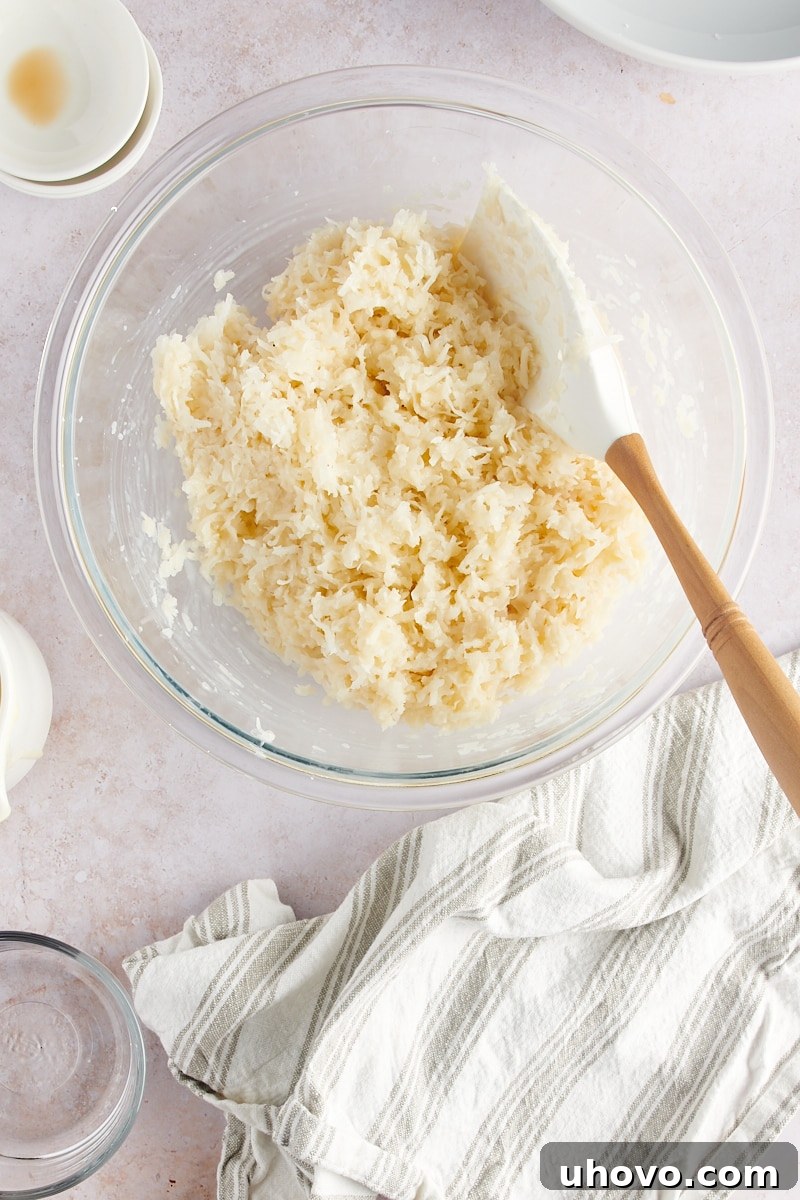 An overhead shot of the fully mixed Coconut Macaroon batter in a clear glass mixing bowl, showcasing its cohesive, sticky texture, ready for portioning.