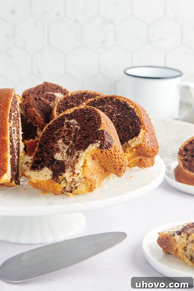 sliced Marble Bundt Cake on a white cake stand, showcasing its beautiful chocolate and vanilla swirls