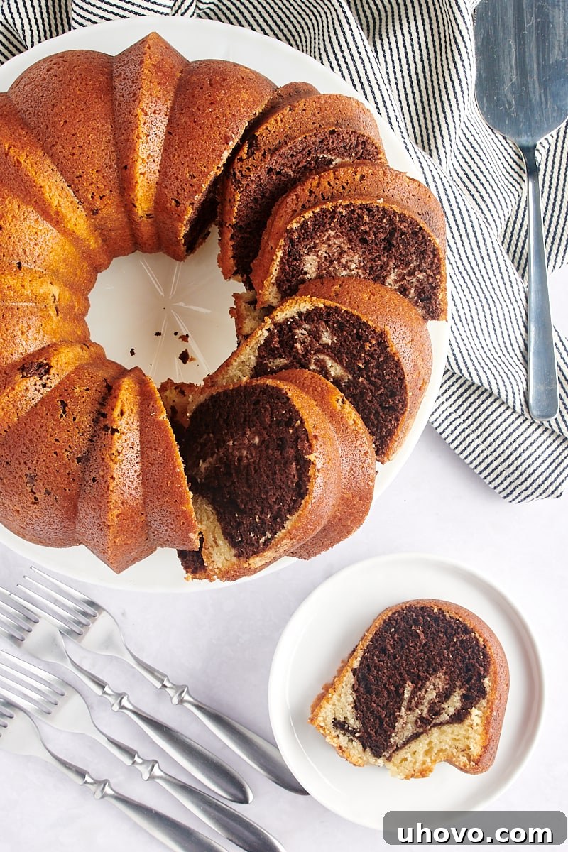 partially sliced Marble Bundt Cake on a white cake stand with a single slice on a white plate
