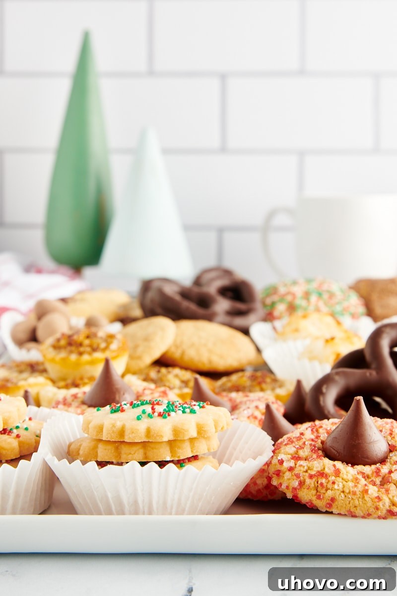 A festive serving tray overflowing with various Christmas cookies and treats, adorned with small wooden Christmas tree decorations in the background.
