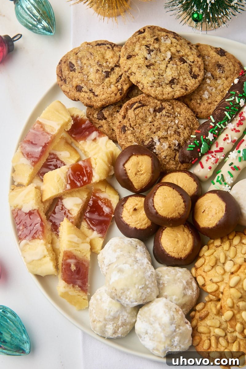 An inviting overhead view of various Christmas cookies and treats artfully arranged on a large white plate, surrounded by sparkling Christmas ornaments.