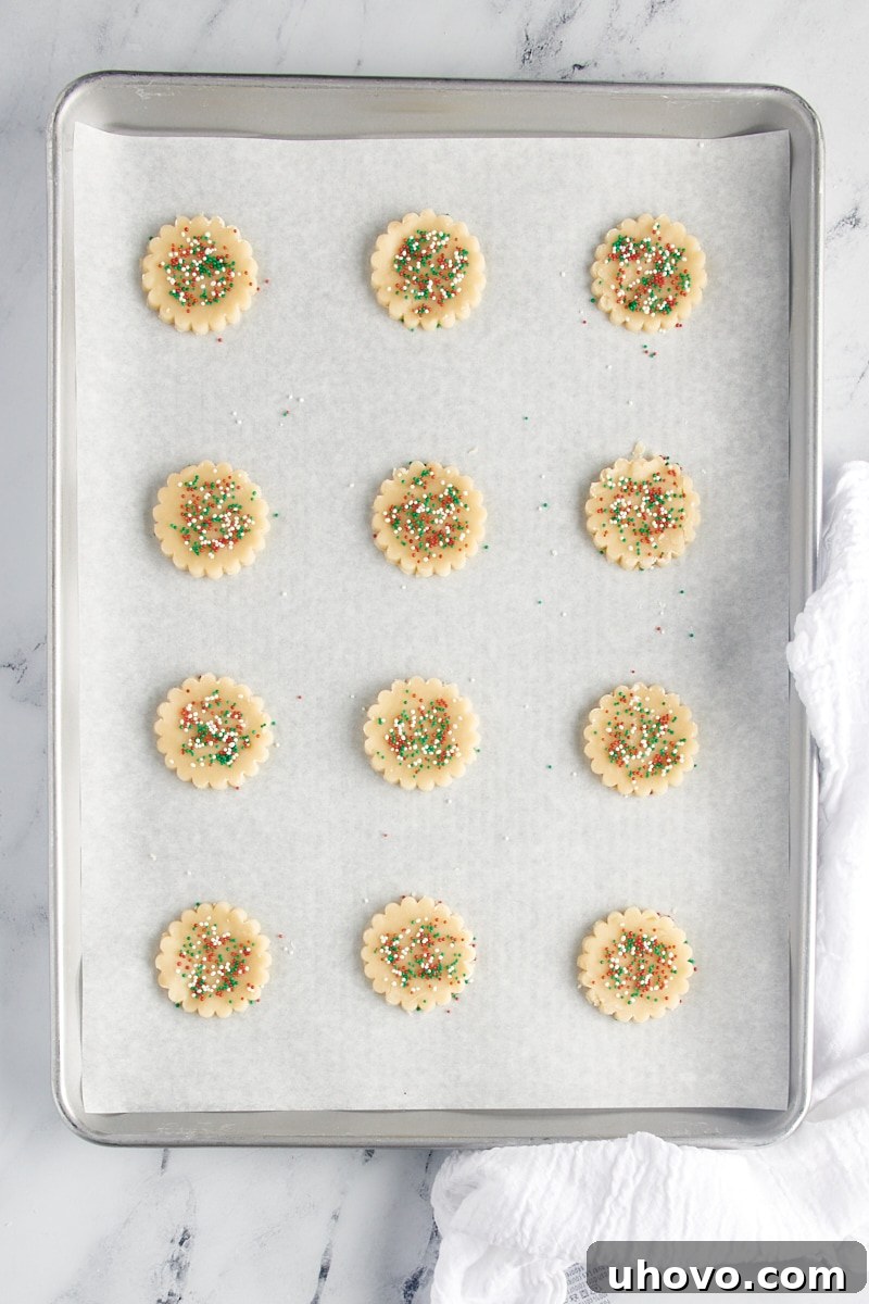 Cutout shortbread cookie dough topped with sprinkles and placed on a parchment-lined baking sheet.