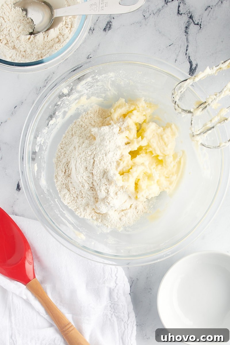 Overhead view of flour added to creamed butter and sugar in a glass mixing bowl.