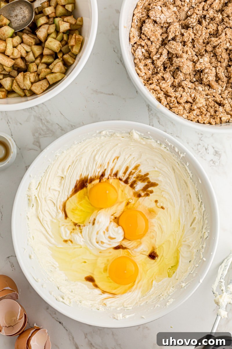 overhead view of eggs and vanilla added to cream cheese and sugar mixture in a white mixing bowl