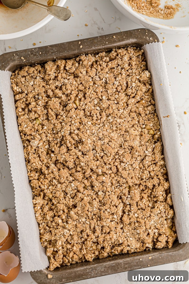 overhead view of streusel topping on top of apples and cheesecake filling in a 9x13 pan