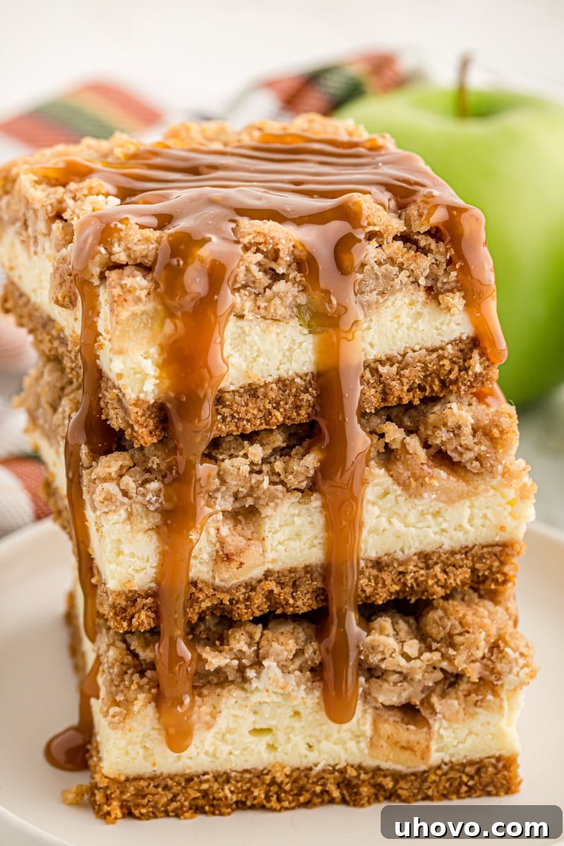 three Caramel Apple Cheesecake Bars stacked on a white plate with caramel sauce drizzled over the top and down the side