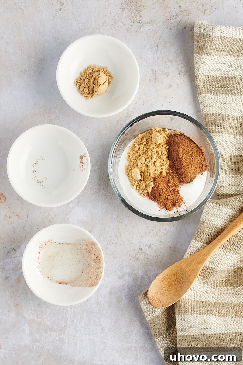 Overhead view of granulated sugar, ground ginger, cinnamon, and nutmeg measured out in a glass mixing bowl, ready to be combined for the coating.