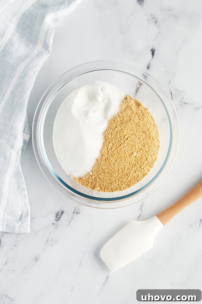 Graham cracker crumbs and granulated sugar mixed in a clear glass bowl, showcasing their fine texture.