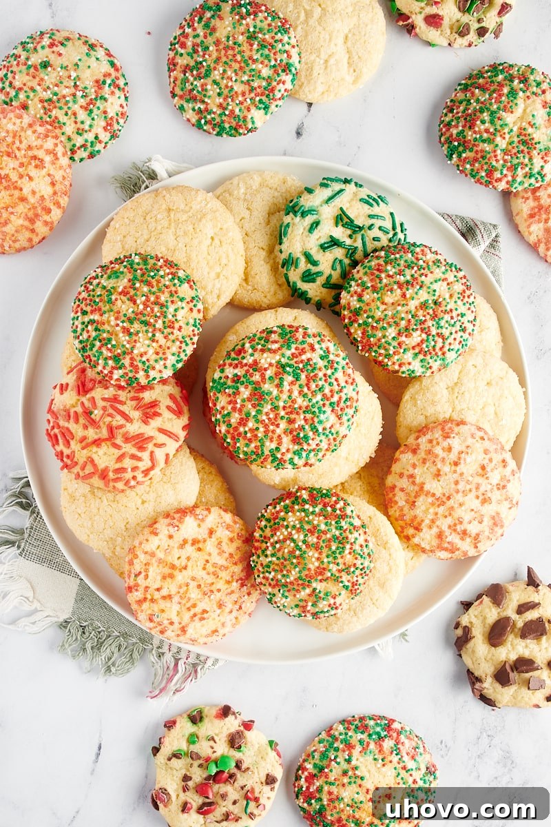 Overhead view of sugar cookies piled on a large white plate with more cookies surrounding the plate.