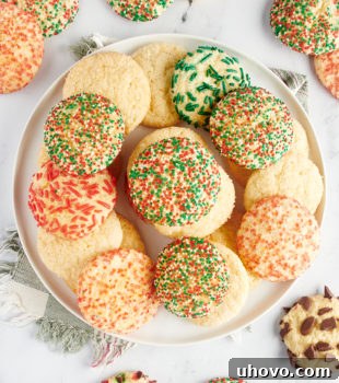 overhead view of sugar cookies piled on a large white plate with more cookies surrounding the plate
