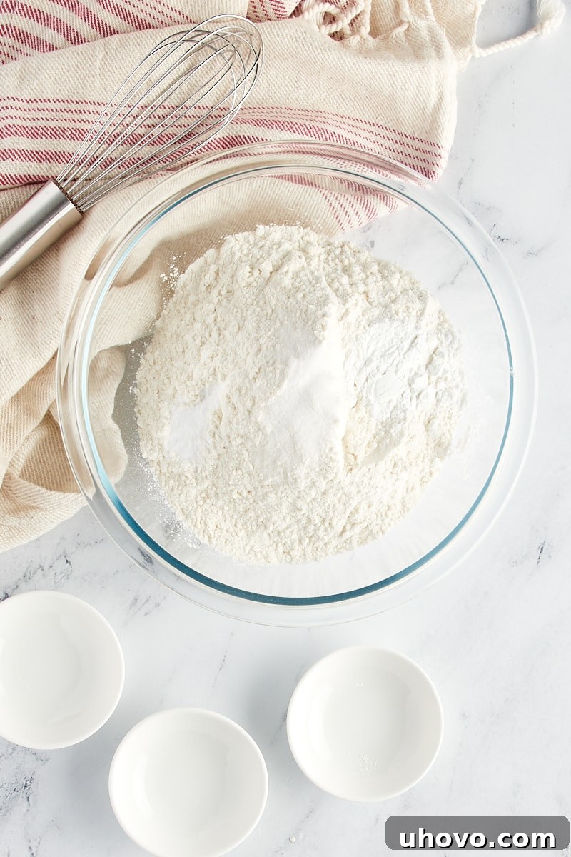 Overhead view of flour, baking powder, baking soda, and salt in a glass mixing bowl.