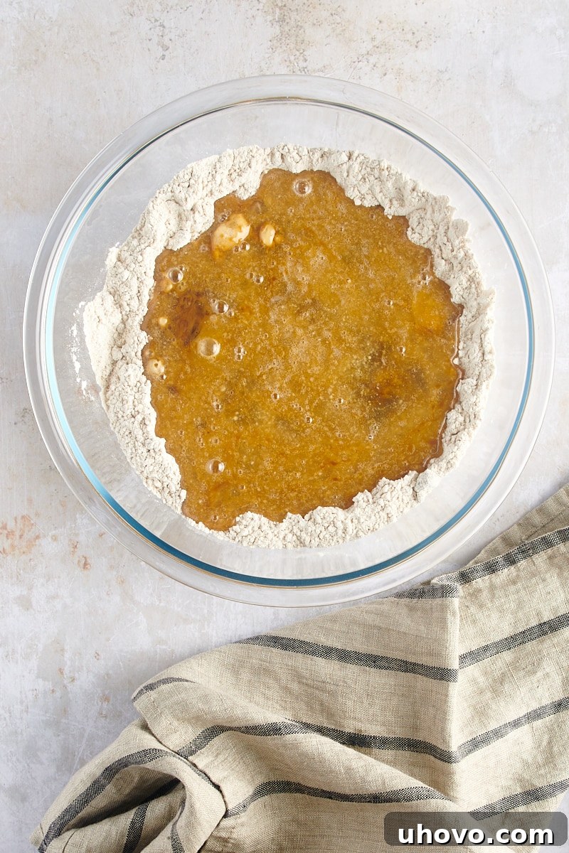 An overhead view capturing the moment when the liquid wet ingredients are poured into the well of the dry ingredients for the gingerbread muffin batter.