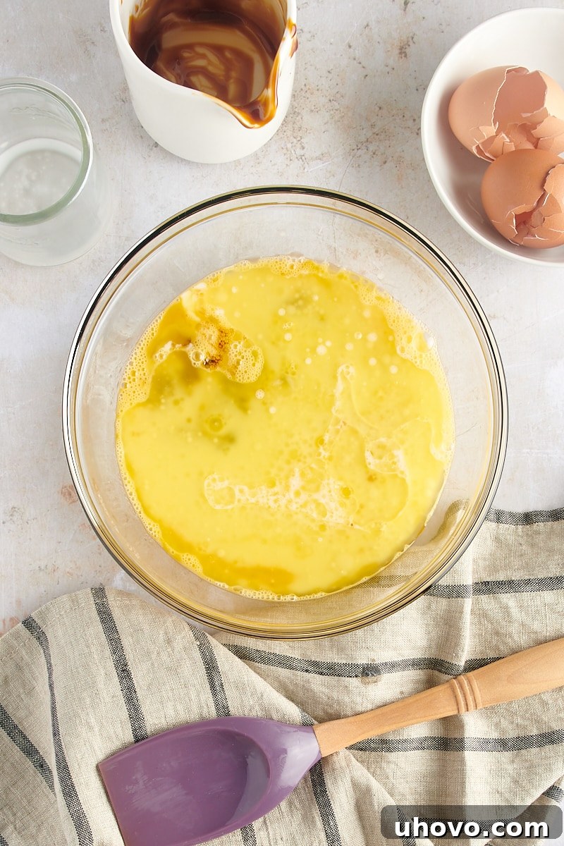 An overhead view of the wet ingredients – room temperature eggs, melted unsalted butter, molasses, and milk – waiting in a clear glass mixing bowl, ready to be combined.
