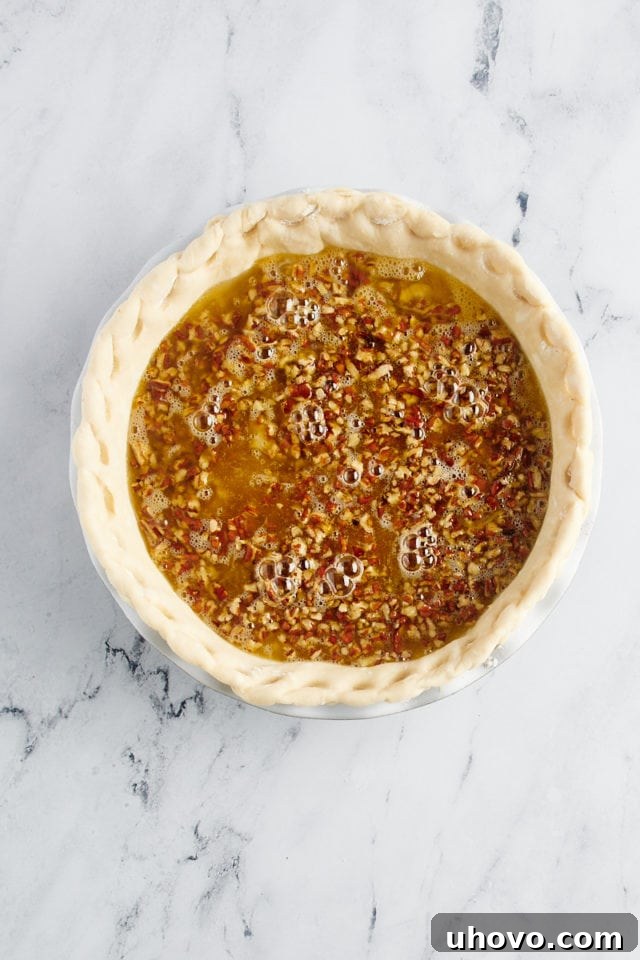 Pouring the pecan pie filling over the layer of pecans and cheesecake in the pie crust.
