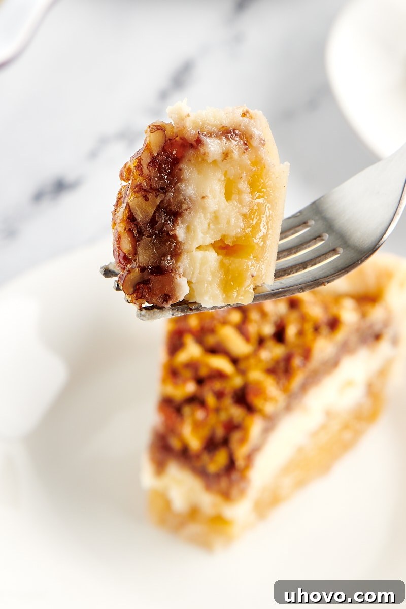 A forkful of Pecan Cheesecake Pie in the foreground, with a remaining slice of pie in the background on a white plate.