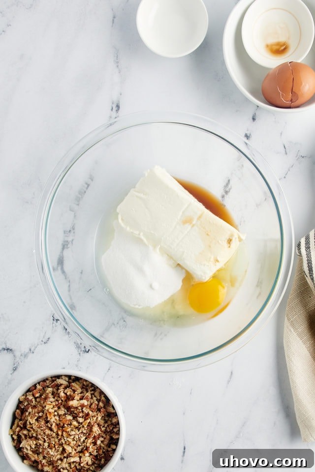 A bowl containing cream cheese, egg, sugar, and vanilla, ready to be mixed.