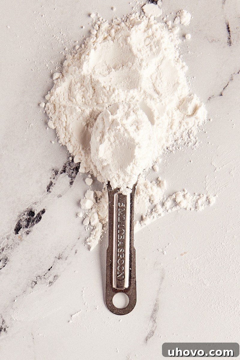 overhead view of baking powder in a measuring spoon and in a pile on a marble surface