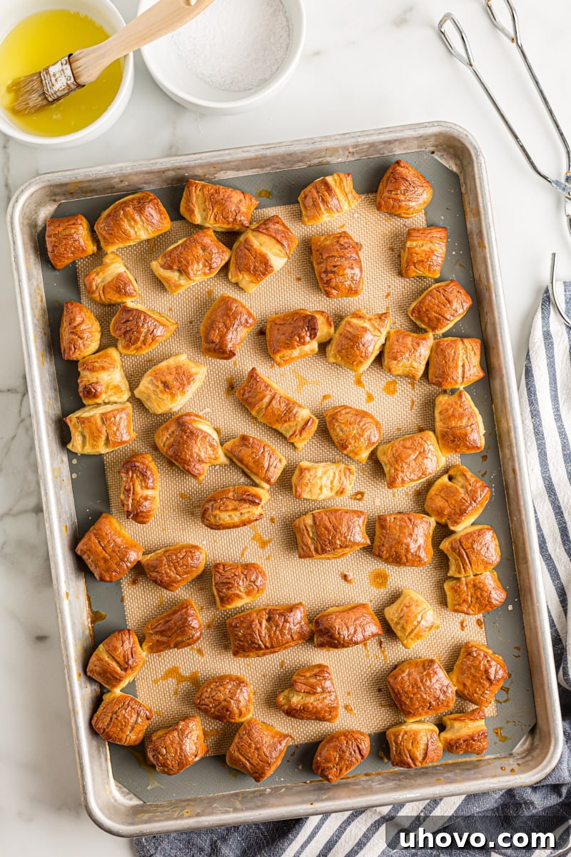A freshly baked batch of golden-brown pretzel bites cooling on a baking sheet lined with parchment paper, perfectly textured and ready for toppings.