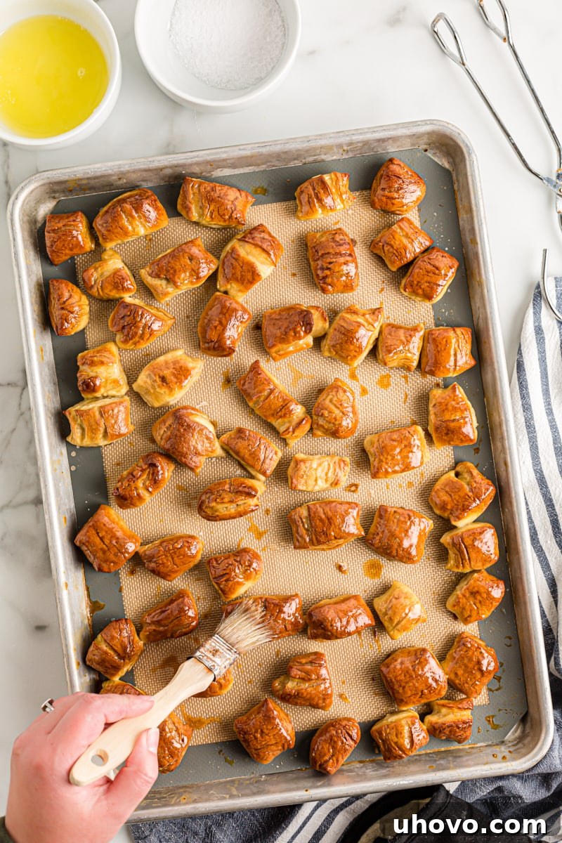 Freshly baked pretzel bites being brushed with melted butter directly on the baking sheet, enhancing their flavor and shine.