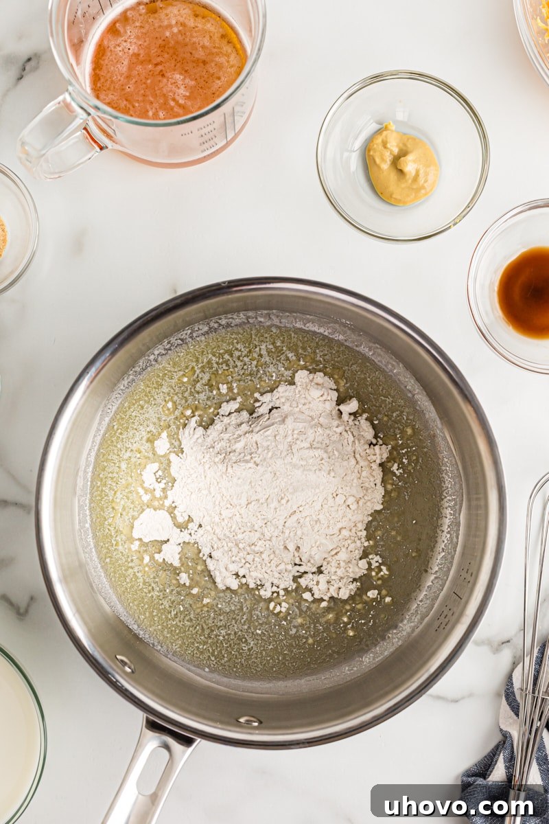 Flour being whisked into melted butter in a medium saucepan, forming the base roux for the beer cheese dip.