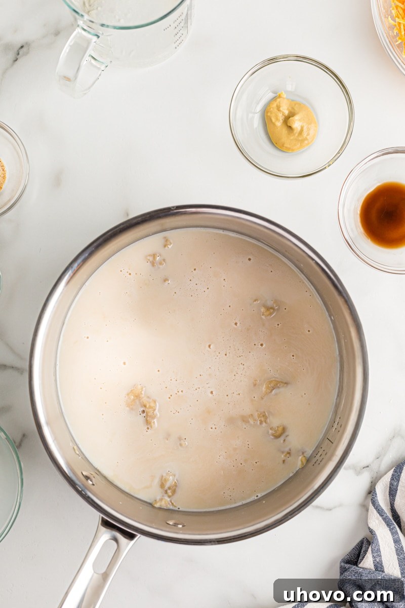 Milk and beer being poured into the butter and flour mixture (roux) in a saucepan, beginning the thickening process for the cheese dip.