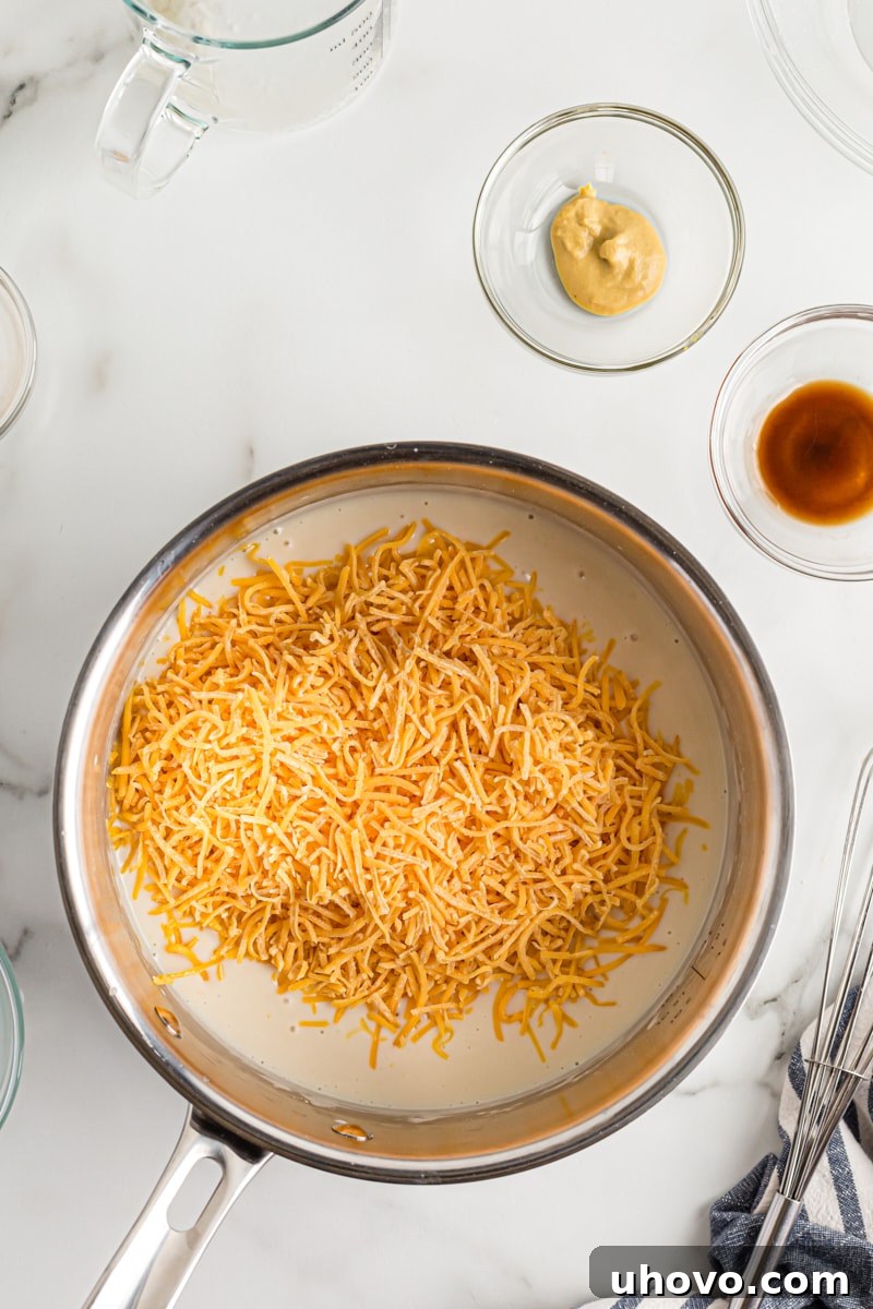 Shredded sharp Cheddar cheese being added to the simmering liquid in a saucepan, melting to create the creamy beer cheese dip.