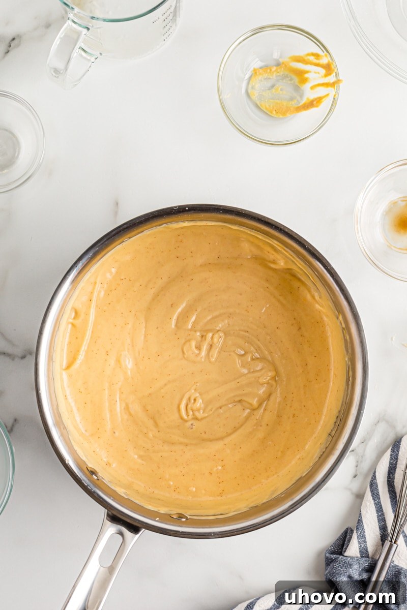 A saucepan filled with a perfectly smooth and creamy finished beer cheese dip, ready to be served with pretzel bites.