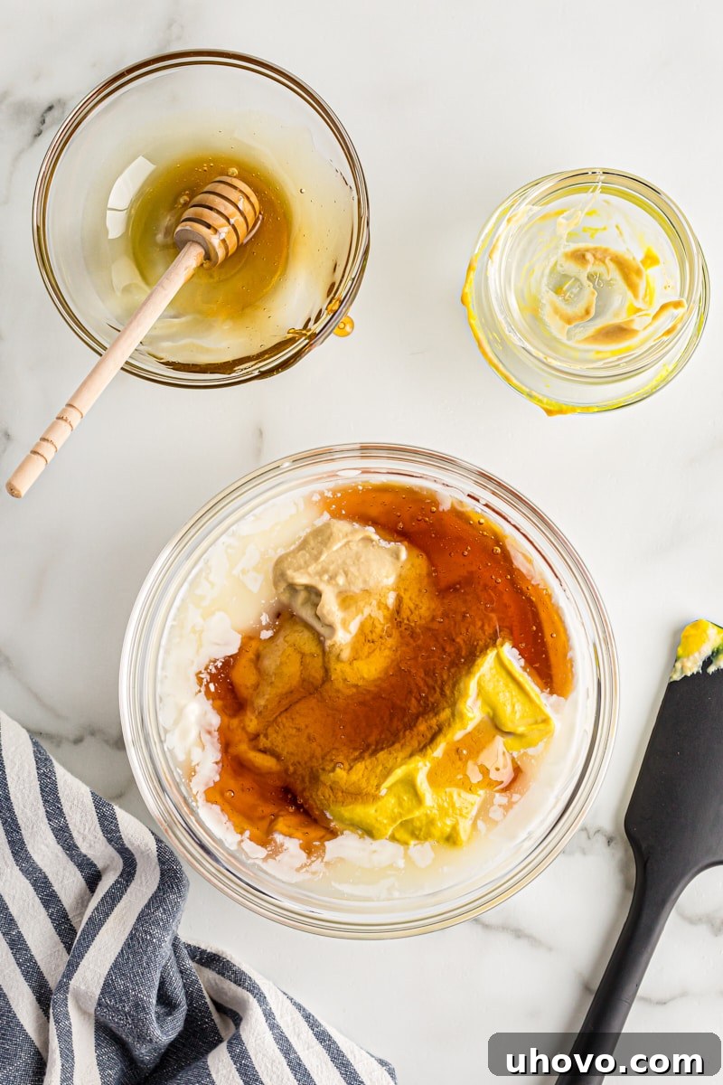 All ingredients for honey mustard dipping sauce being whisked together in a glass mixing bowl until smooth.
