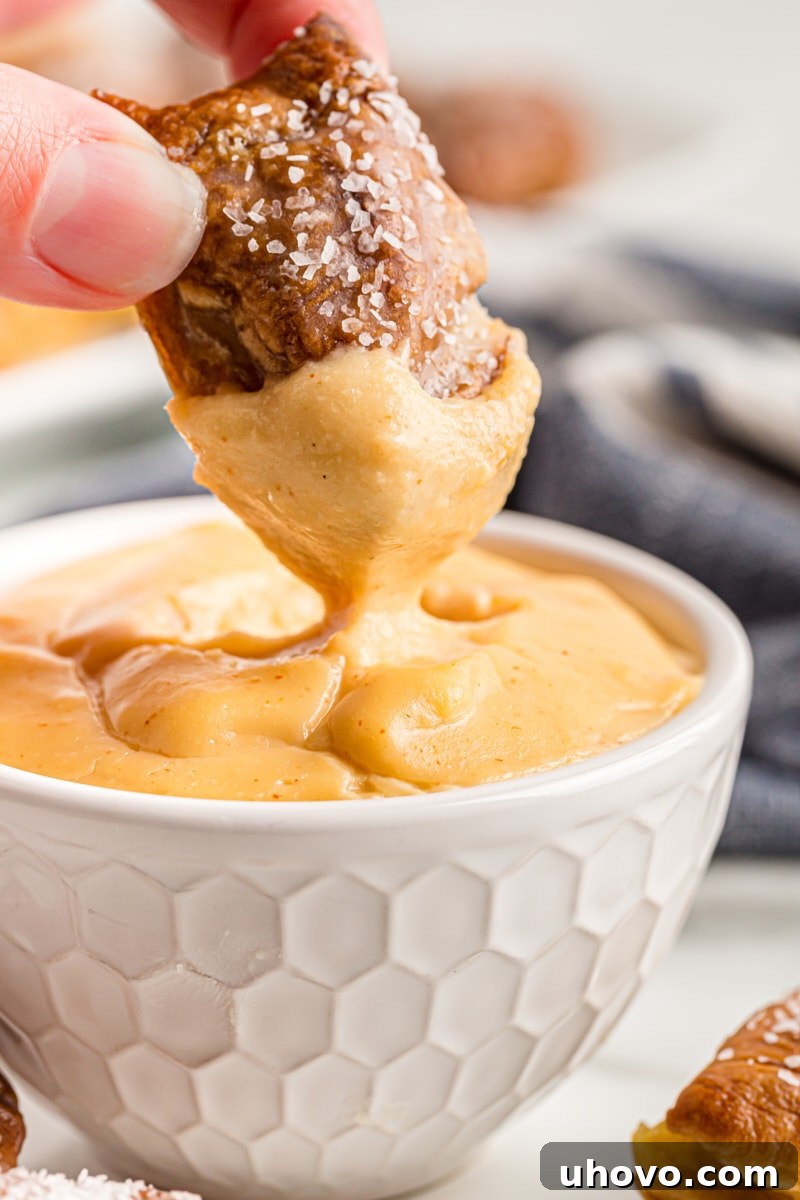 A close-up shot of a pretzel bite being dipped into a rich, creamy beer cheese dip, highlighting the appetizing texture.