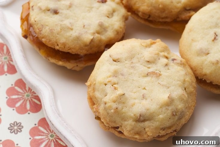 Stacked almond and apricot sandwich cookies on a white serving plate, featuring a golden cookie base and a vibrant orange filling.