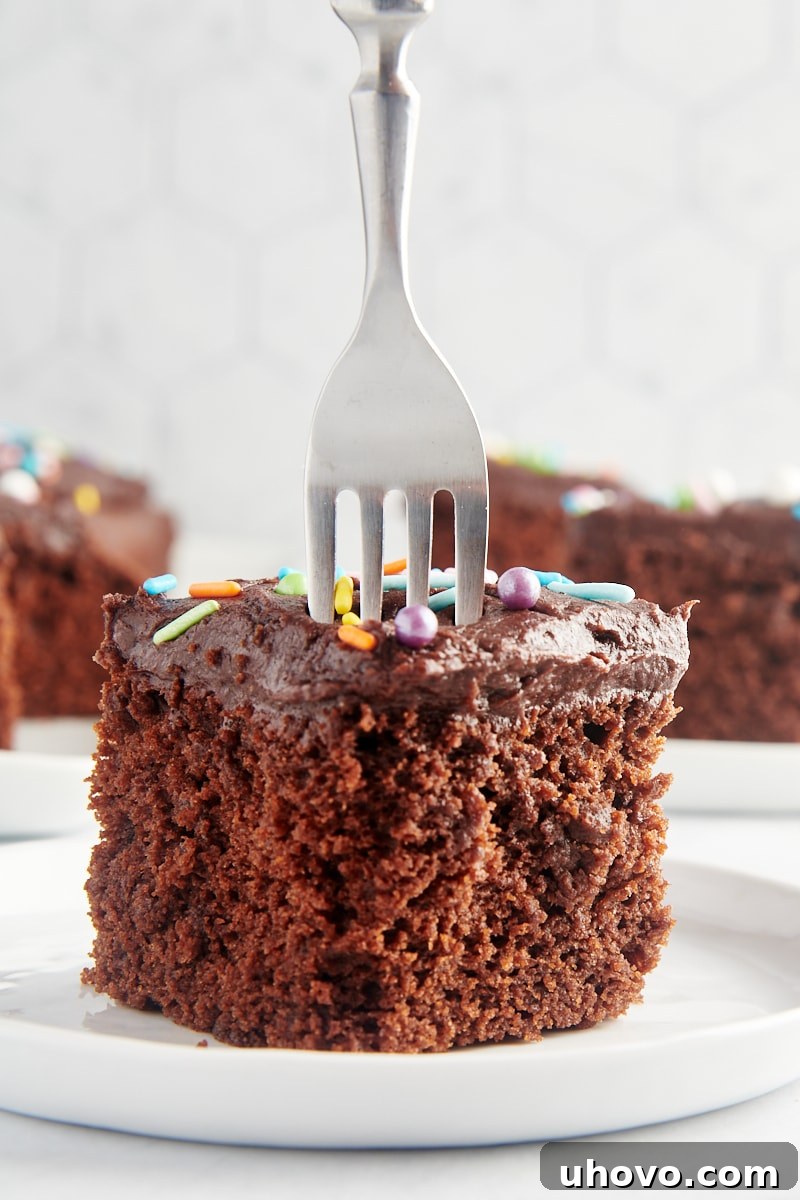 a fork cutting into a slice of Chocolate Sheet Cake on a white plate