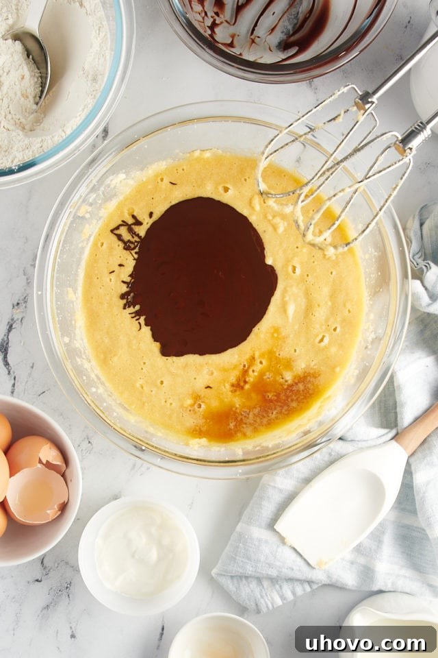 overhead view of melted chocolate and vanilla extract added to cake batter in a glass mixing bowl