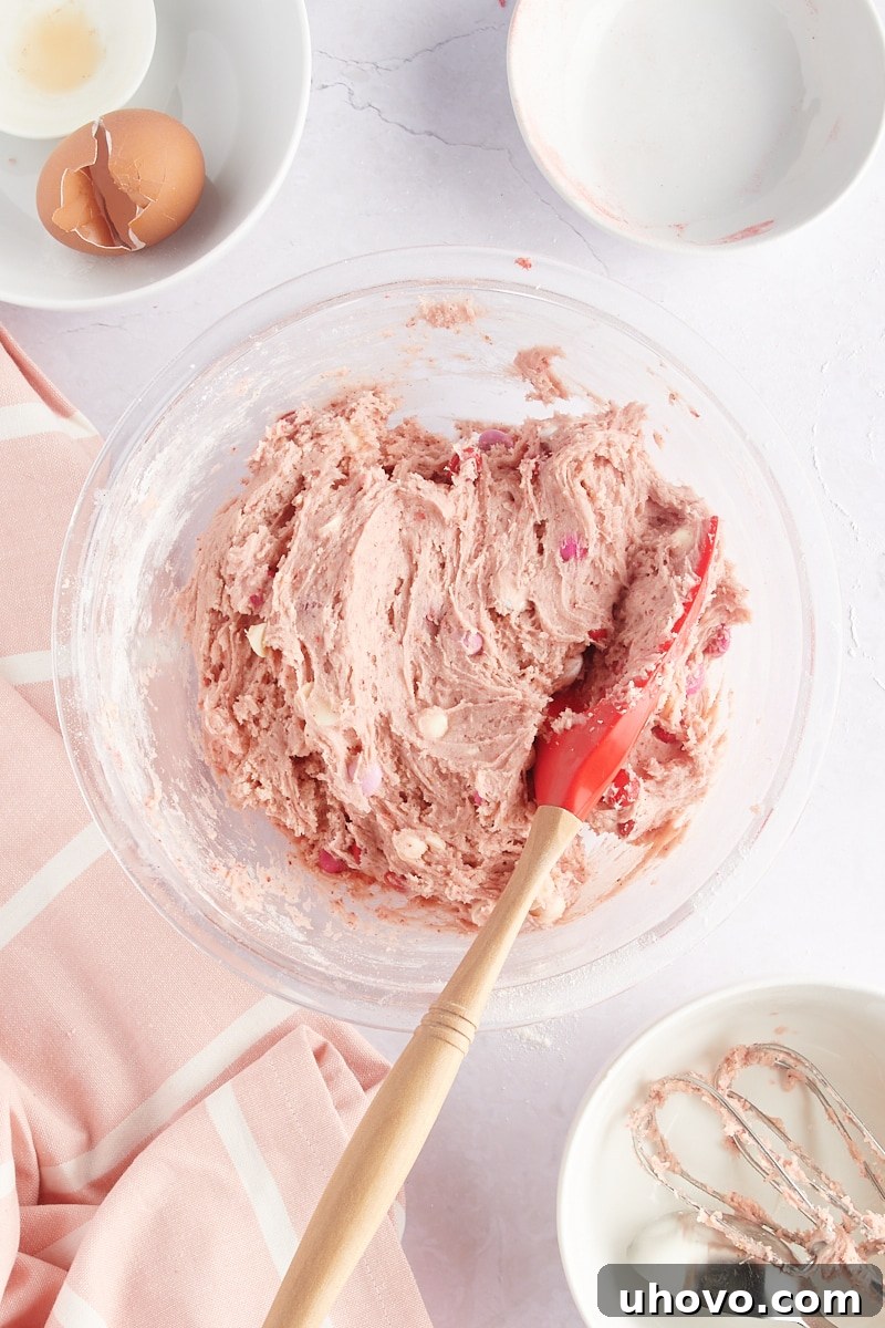overhead view of mixed Strawberry M&M Cookie dough in a glass mixing bowl