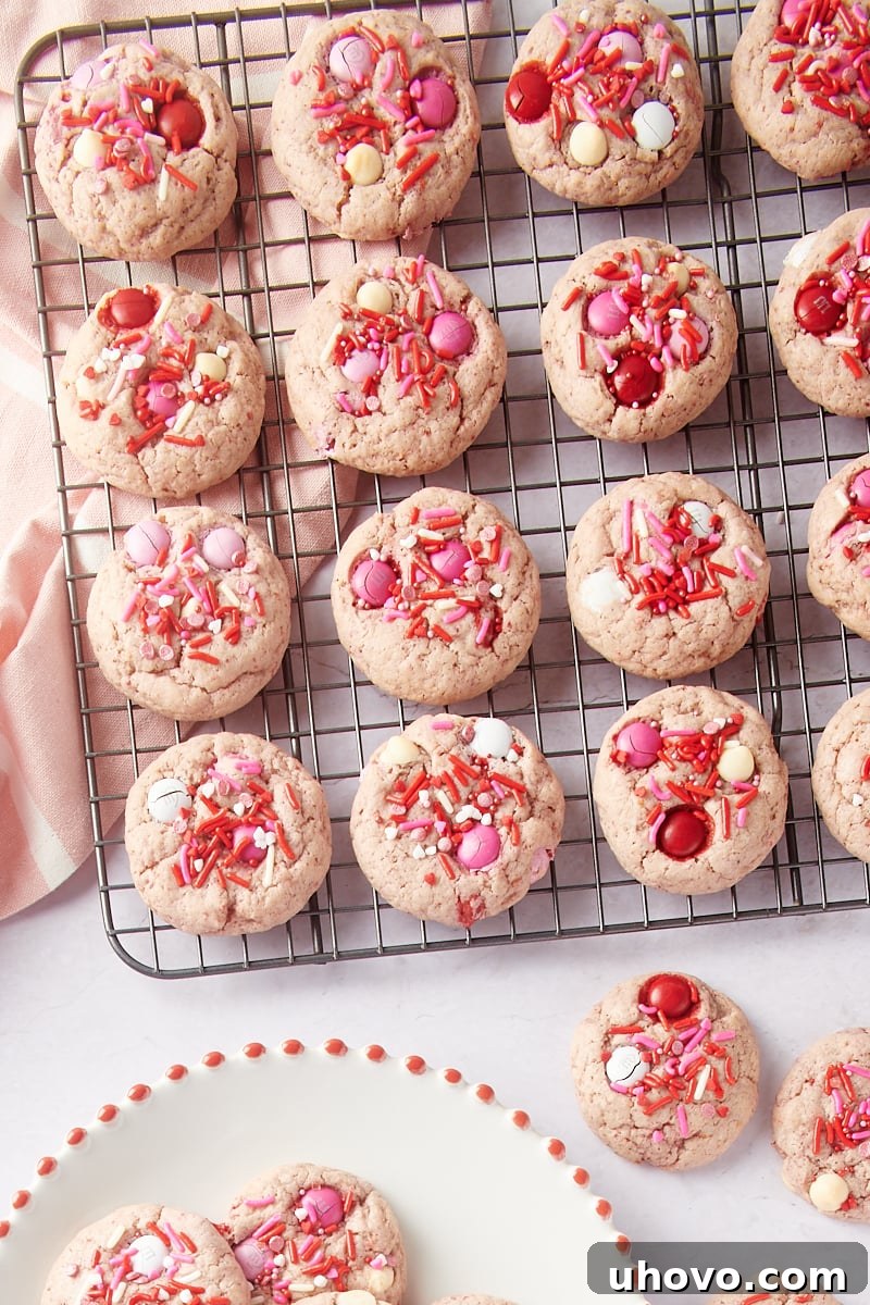 Strawberry M&M Cookies on a wire rack and on a white place and marble surface