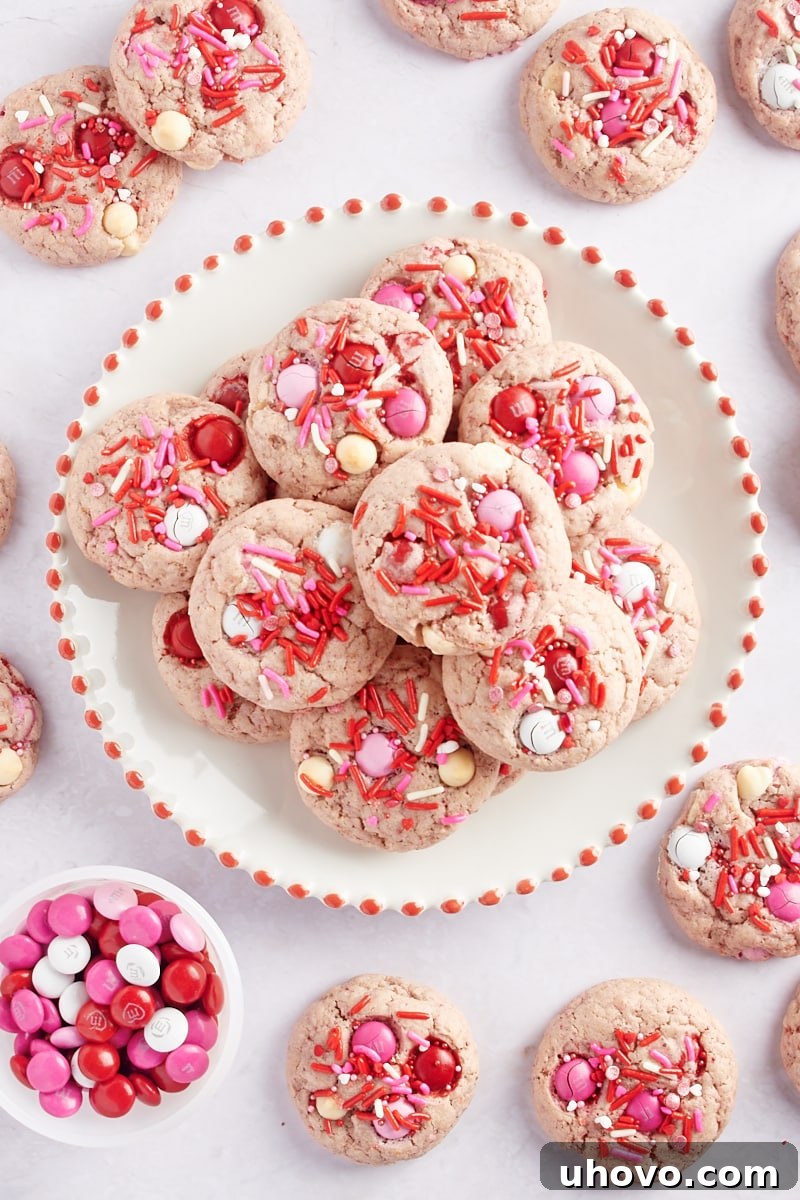 overhead view of Strawberry M&M Cookies on a red-rimmed white plate with more cookies around the plate