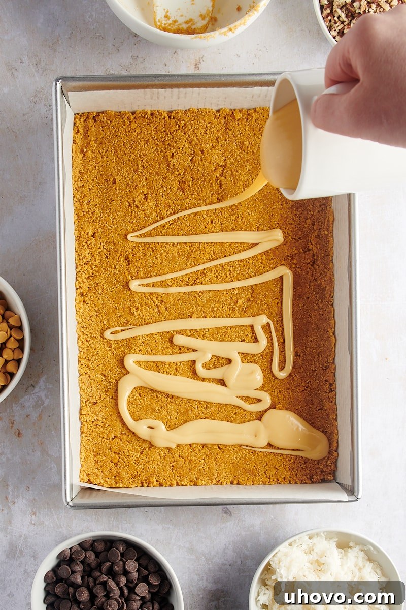 Pouring sweetened condensed milk over graham crust in baking pan for seven layer bars