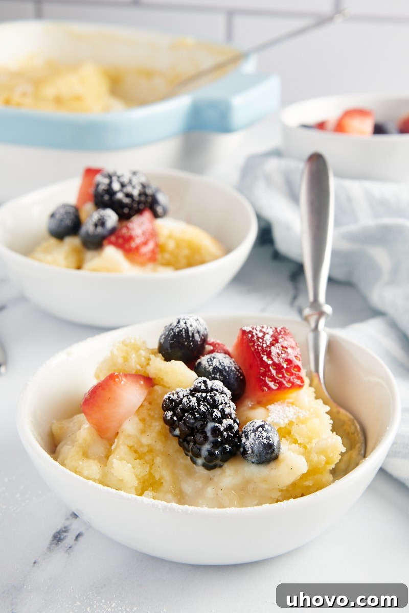 A delectable individual serving of Vanilla Pudding Cake, garnished with vibrant fresh berries and a light dusting of confectioners' sugar, presented in an elegant white bowl.
