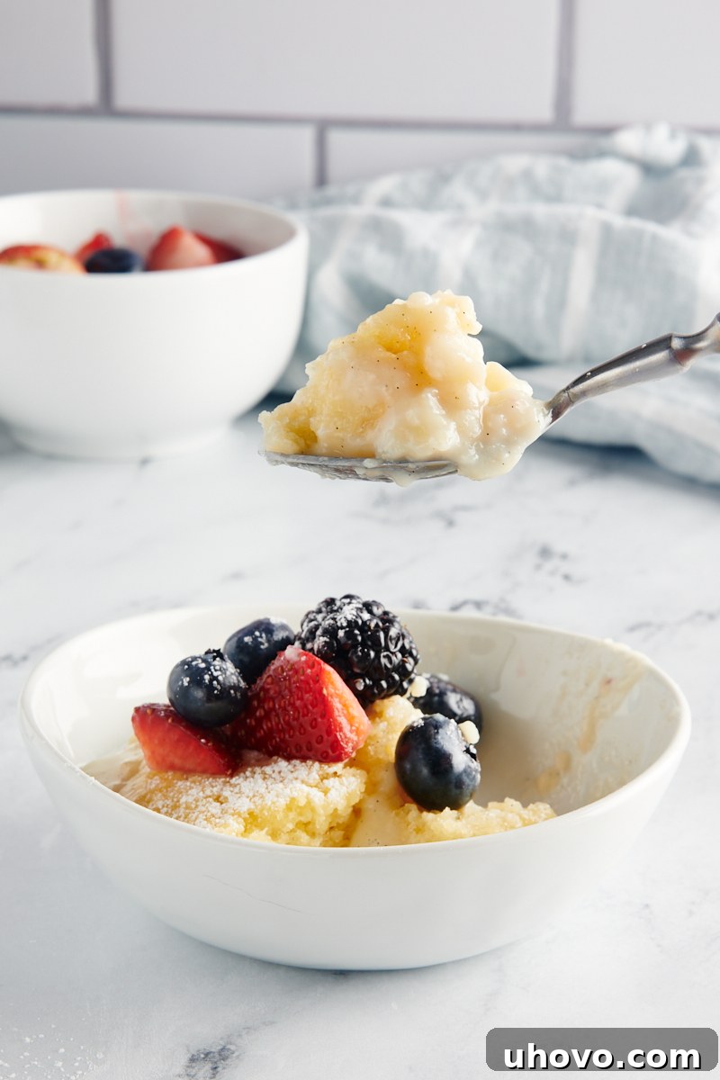A tantalizing bite of Vanilla Pudding Cake perfectly poised on a spoon, hovering above a serving bowl generously topped with a medley of fresh berries, highlighting the cake's tender texture and the luscious sauce.