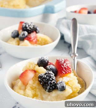 a bowl of Vanilla Pudding Cake served in a white bowl and topped with fresh berries and confectioners' sugar