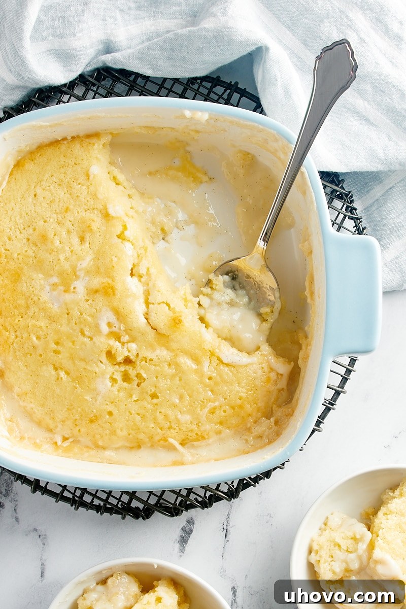 A tempting overhead view of a freshly baked Vanilla Pudding Cake still in its baking pan, with a few generous servings already taken, revealing the luscious sauce underneath.