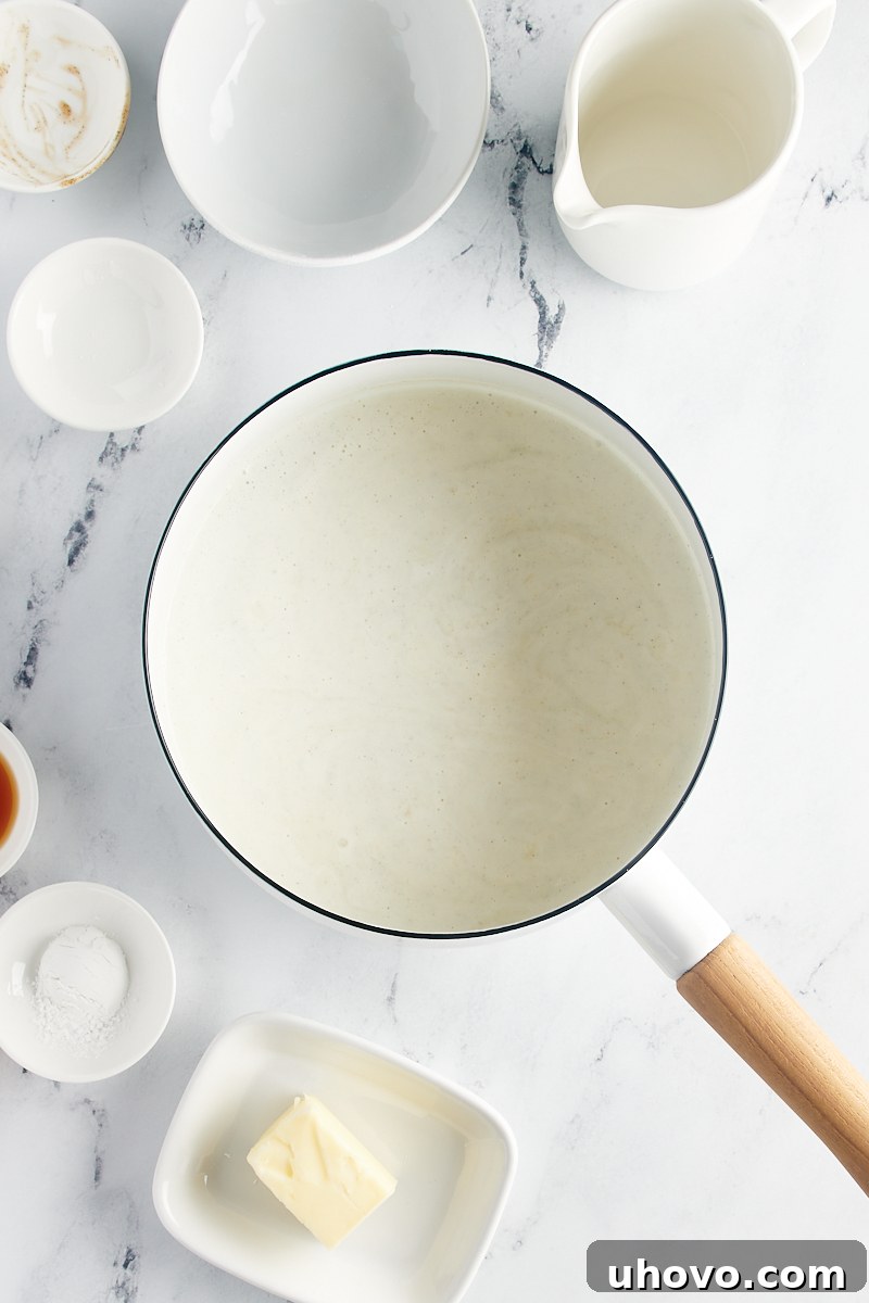 A close-up view of the vanilla pudding sauce gently simmering in a saucepan, showing its slight thickening.