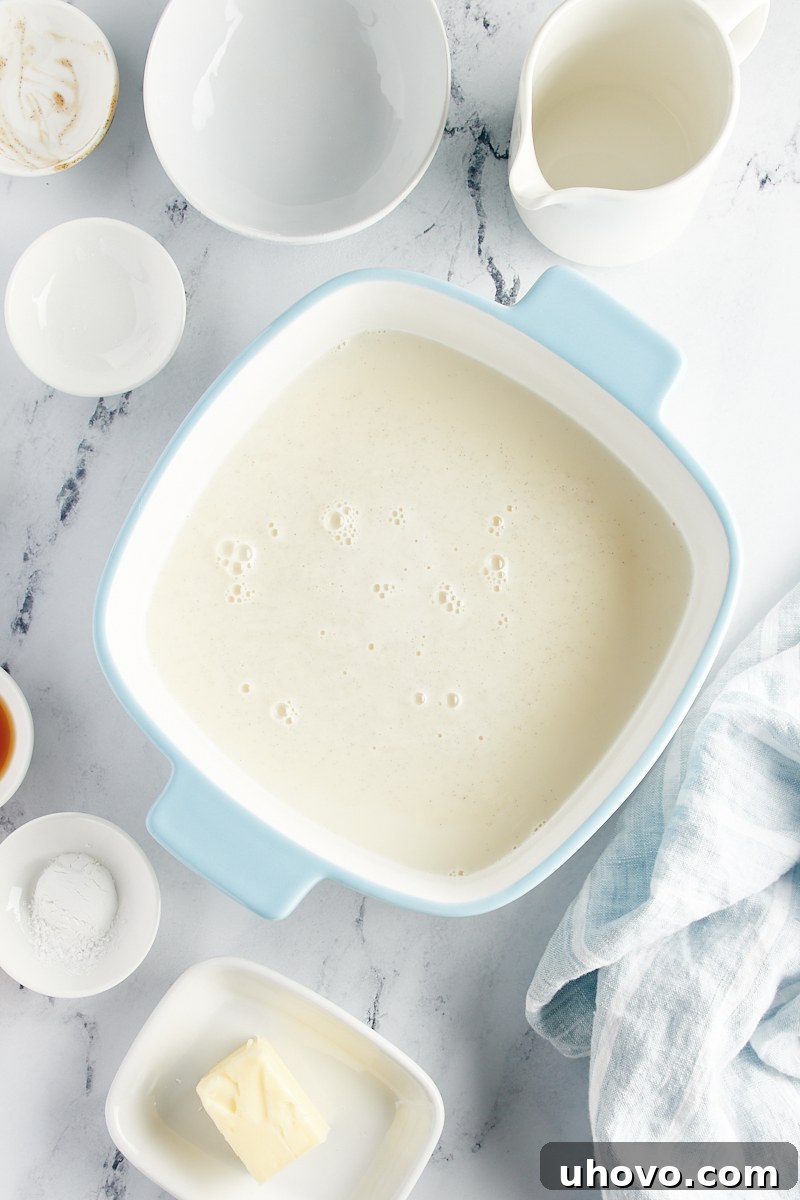 The thickened vanilla pudding sauce evenly poured into the prepared baking pan, forming the bottom layer.
