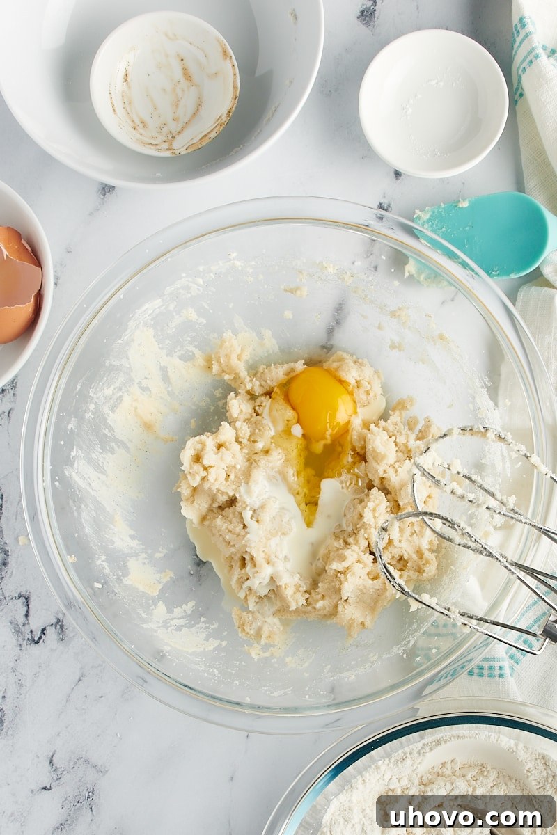 Overhead view of an egg added to a mixing bowl with butter and sugar.